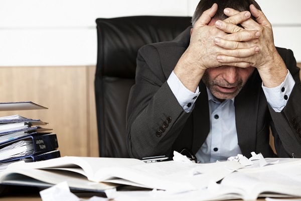 Homme qui semble dépité devant un bureau remplit de papiers et documents